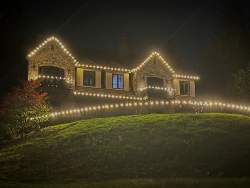 Stone house on a hill with warm white C9 bulbs along every roofline, balcony and fence